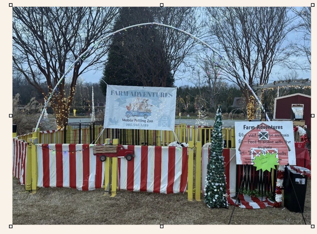 Farm Adventures mobile petting zoo setup with banner, pricing sign, and holiday lights at dusk